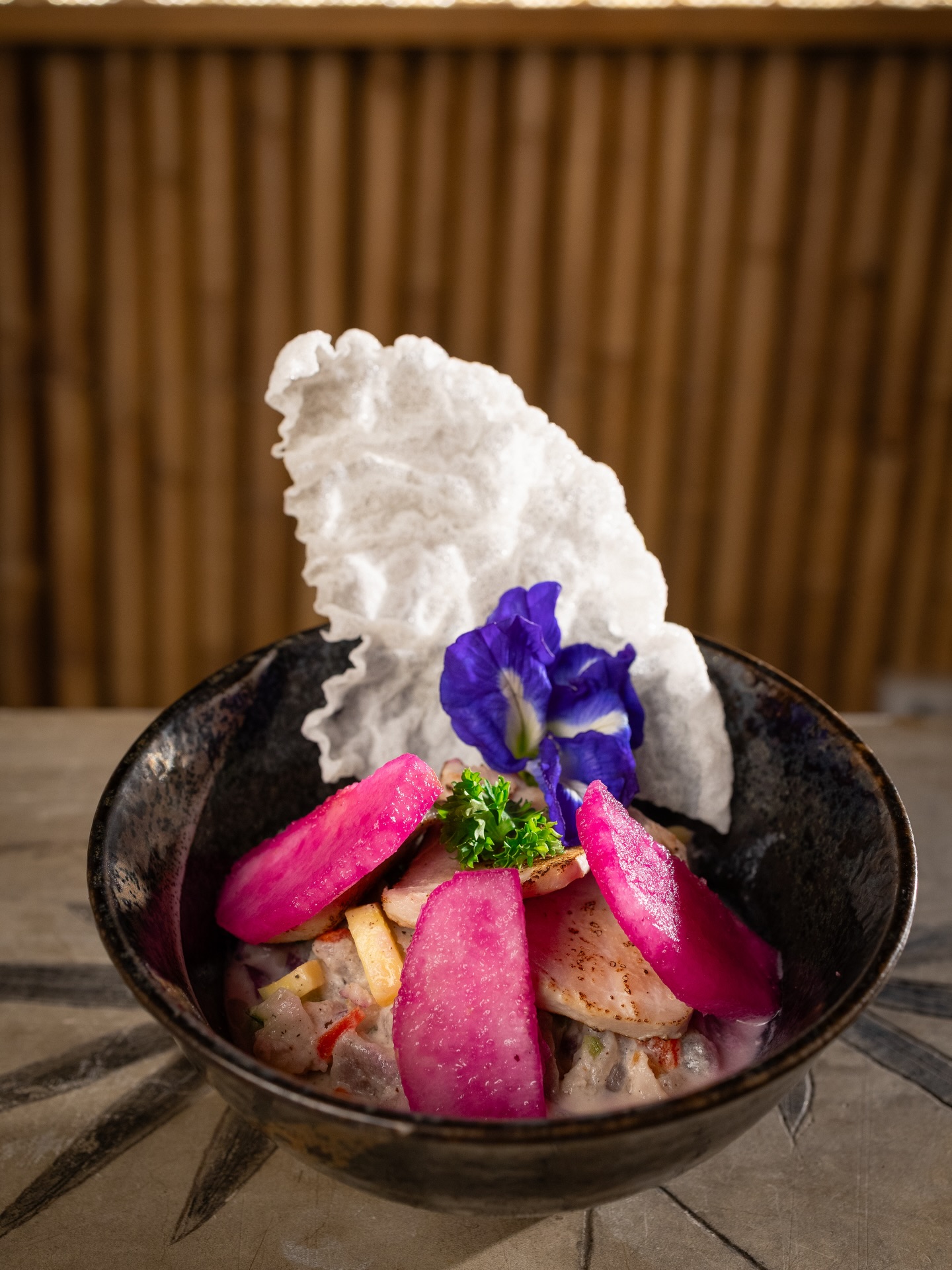 Ceviche in a dark bowl with butterfly pea flower