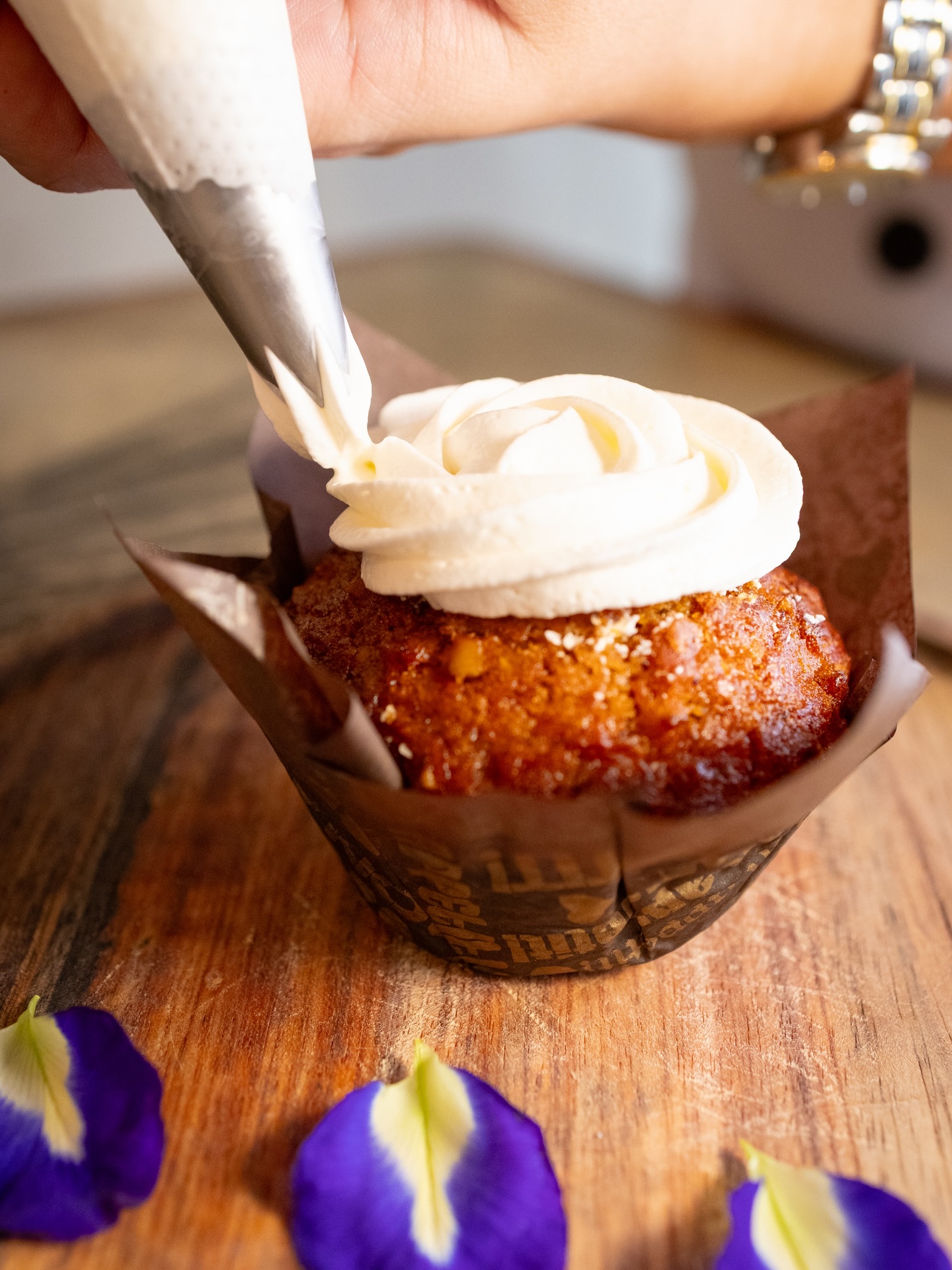 Cupcake being frosted with cream on a wood board